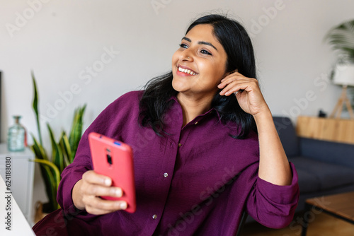 Happy relaxed young indian woman using cell phone while relaxing at home Fototapet