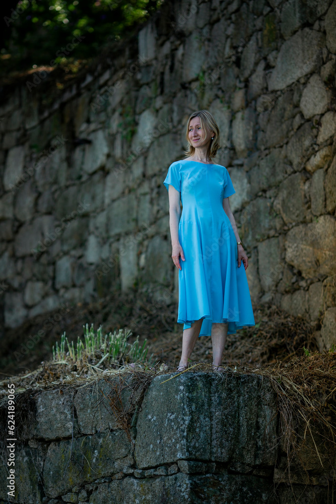 A woman dressed in blue stands in the ruins of a medieval fortress.