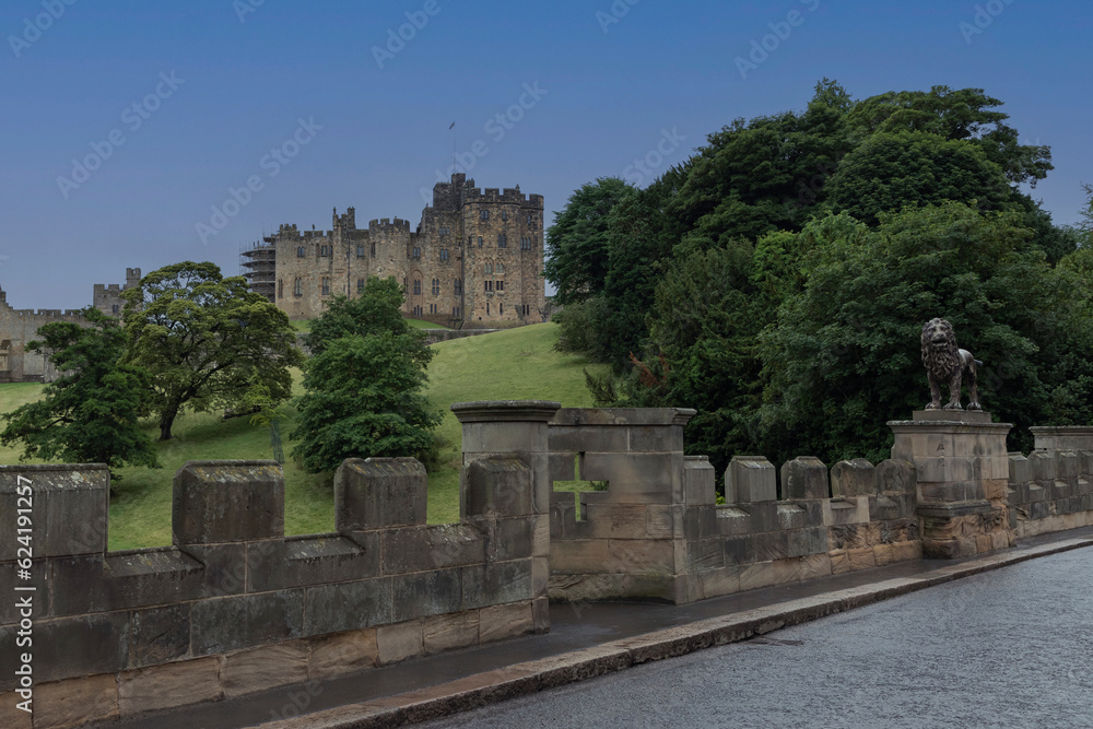 Obraz premium Looking at Alnwick Castle off a bridge with a lion statue