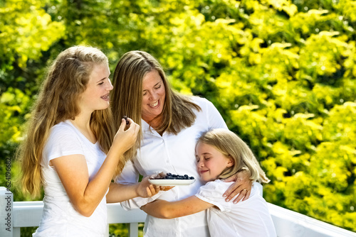 Mother and her daughters enjoying being outdoors while eating fresh blueberry fruit