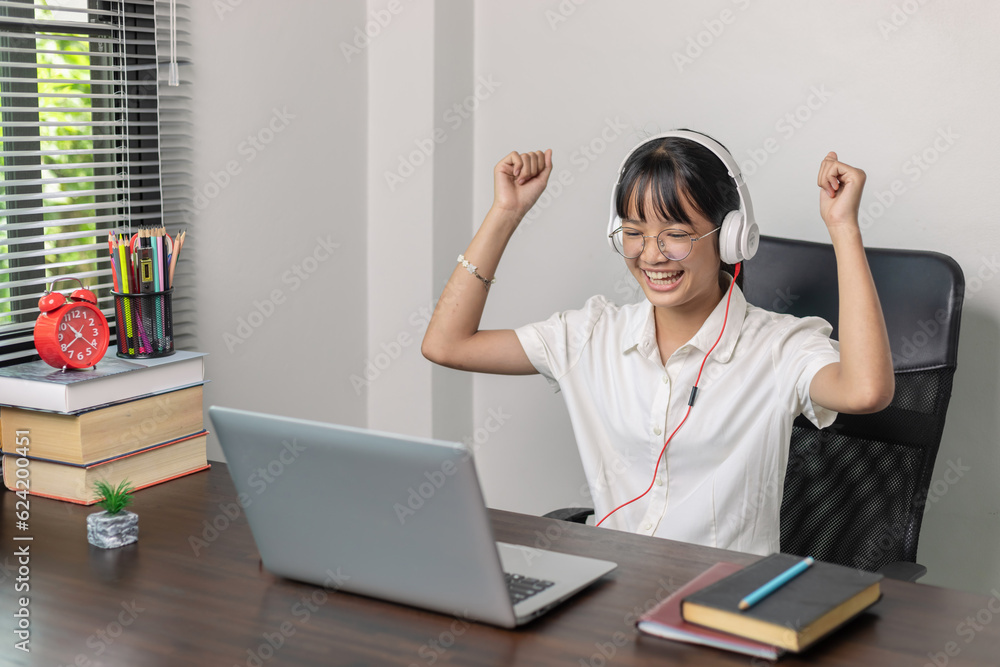 Success cheerful smiling asian teen girl with glasses and wearing headphones having fun looking at laptop computer. Success cheerful smiling asian teen girl with glasses and wearing headphones having fun looking at laptop computer.