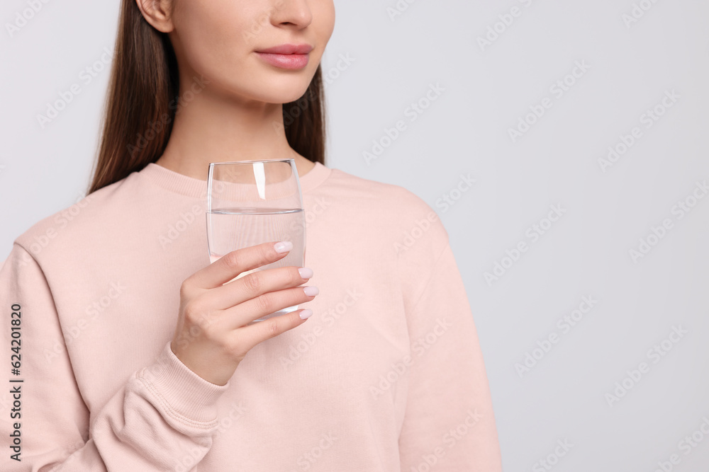Healthy habit. Woman holding glass with fresh water on light grey background, closeup. Space for text Healthy habit. Woman holding glass with fresh water on light grey background, closeup. Space for text