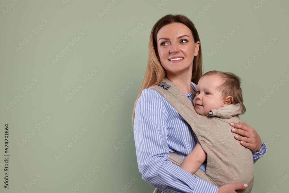 Mother holding her child in sling (baby carrier) on olive background. Space for text Mother holding her child in sling (baby carrier) on olive background. Space for text