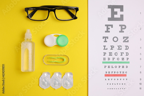 Vision test table, glasses and contact lenses on a colored background.