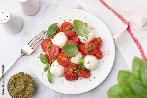 Tasty salad Caprese with tomatoes, mozzarella balls and basil served on white marble table, flat lay