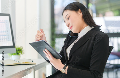 Busy young female employee having phone conversation and checking information on digital tablet.
