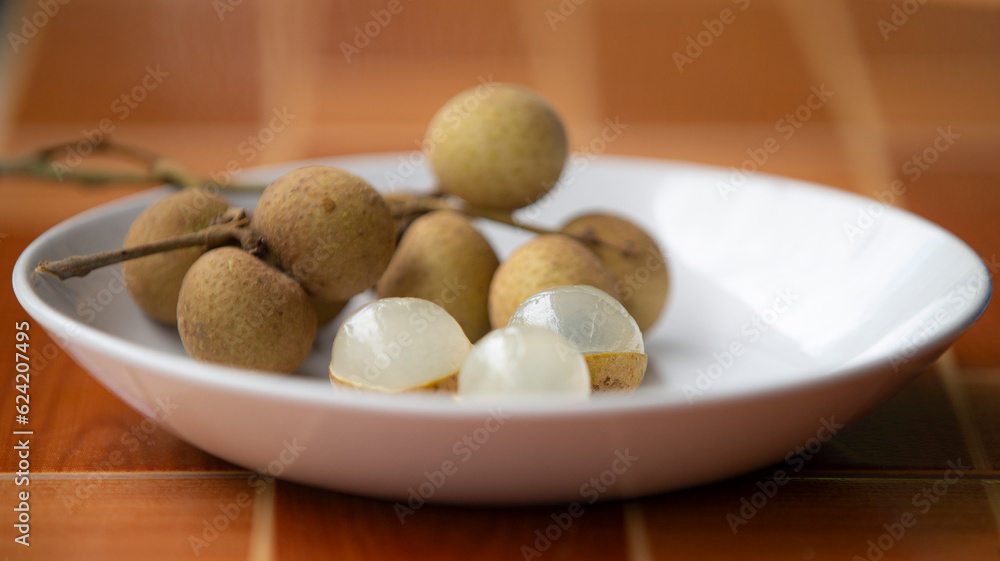 Longan fruit in a white plate on a brown wooden table. Longan fruit in a white plate on a brown wooden table.