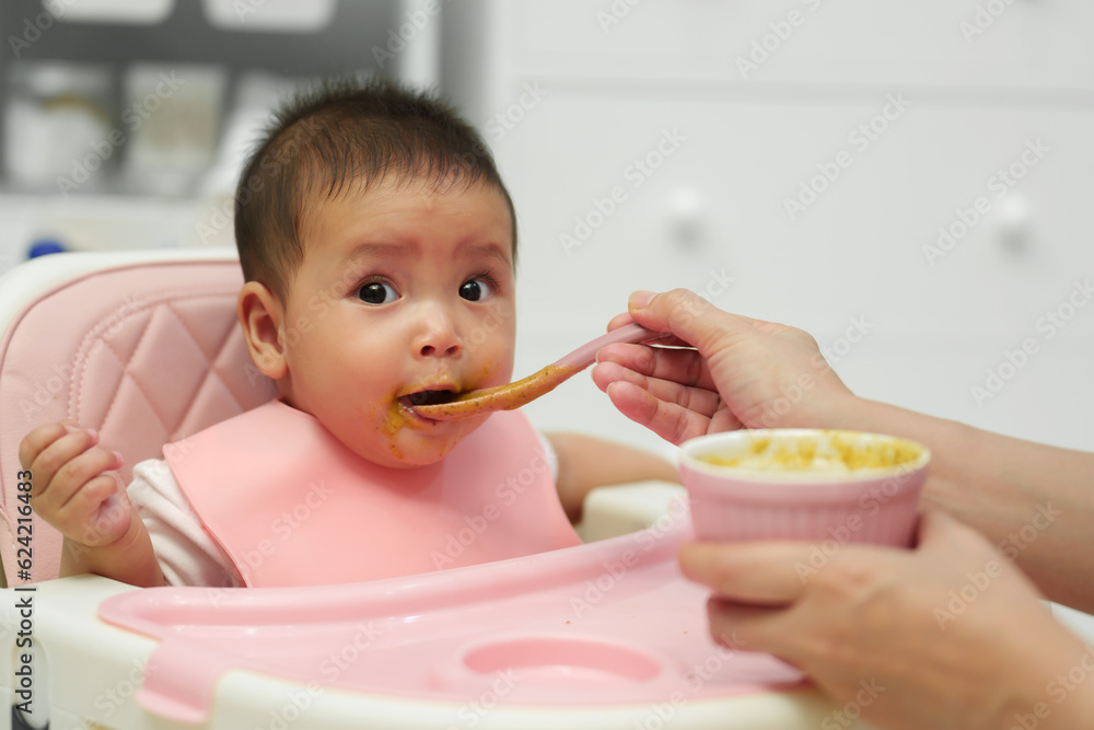 mother feeding food to her infant baby eating with spoon at home mother feeding food to her infant baby eating with spoon at home