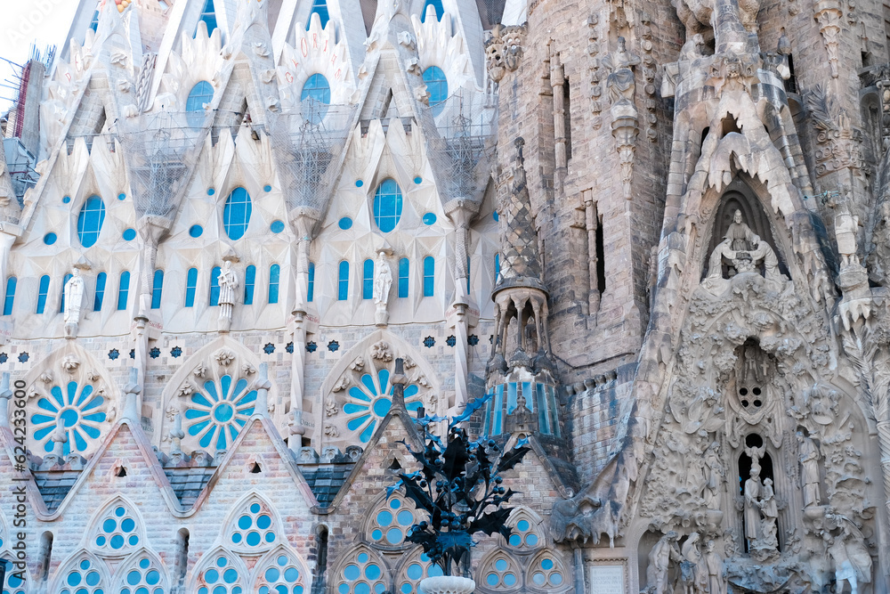 Barcelona, Spain, May 27 2022. Close-up of the facade of the famous Sagrada Familia Cathedral. The blue sky is reflected in the stained glass windows.