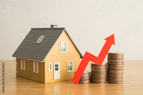 Red graph chart rising up on stack coins and house model on wooden table white wall background. Concept of money management for mortgage loan, fed increase interest rate, real estate price increase.