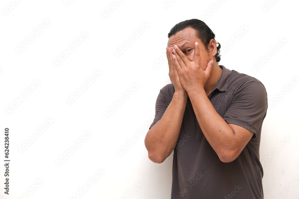 Asian man's expression is peeking from between the fingers Asian man's expression is peeking from between the fingers