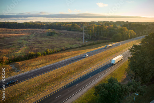 Aerial view of busy american highway with fast moving traffic surrounded by fall forest trees. Interstate transportation concept