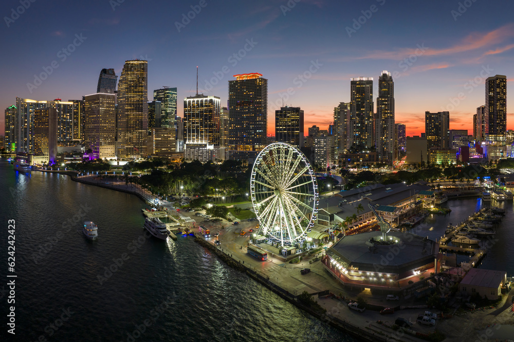 Fototapeta premium Aerial view of Skyviews Miami Observation Wheel at Bayside Marketplace with reflections in Biscayne Bay water and high illuminated skyscrapers of Brickell, city's financial center at night