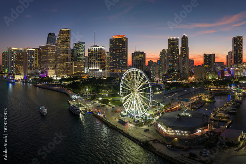 Aerial view of Skyviews Miami Observation Wheel at Bayside Marketplace with reflections in Biscayne Bay water and high illuminated skyscrapers of Brickell, city's financial center at night