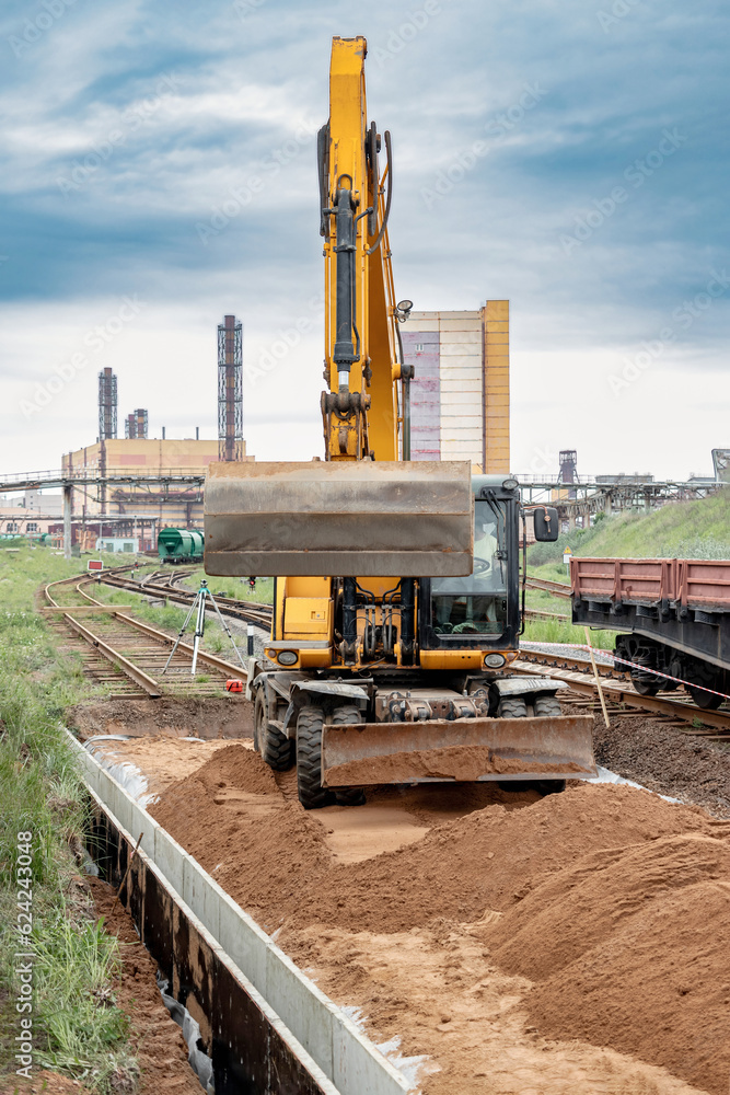 A powerful wheeled excavator prepares the site for the construction of the railway. Excavator with a wide bucket leveling the surface of the railway track. Excavation. A powerful wheeled excavator prepares the site for the construction of the railway. Excavator with a wide bucket leveling the surface of the railway track. Excavation.