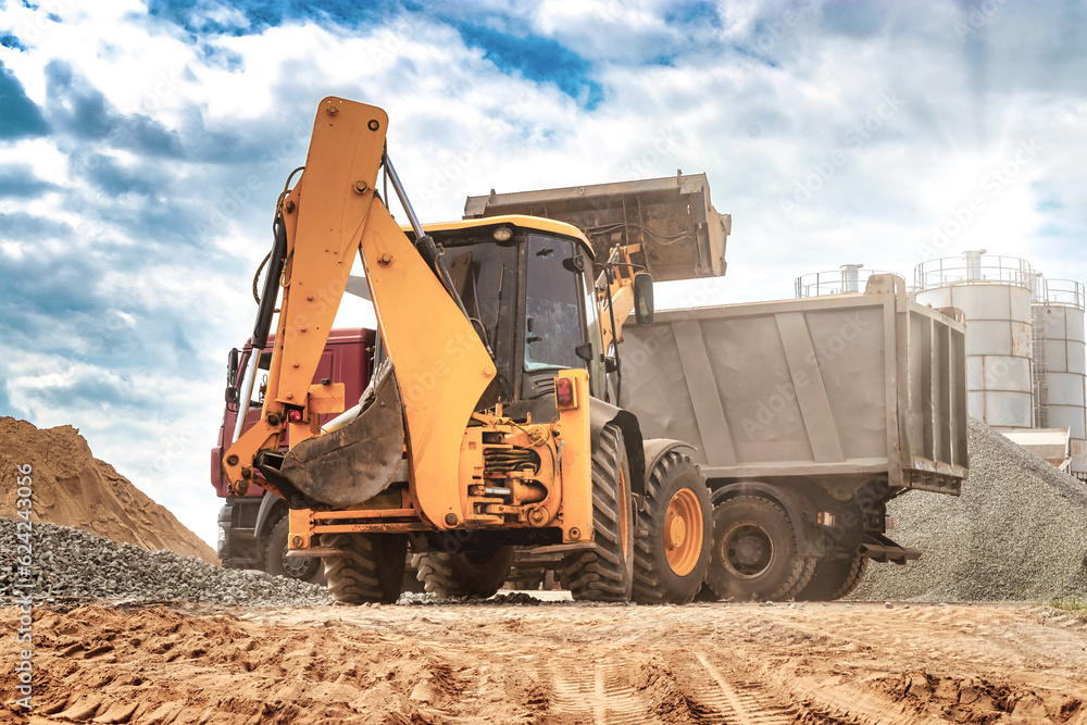 A universal loader or excavator loads sand or grain into a dump truck. Powerful modern equipment for earthworks and moving bulk cargo.