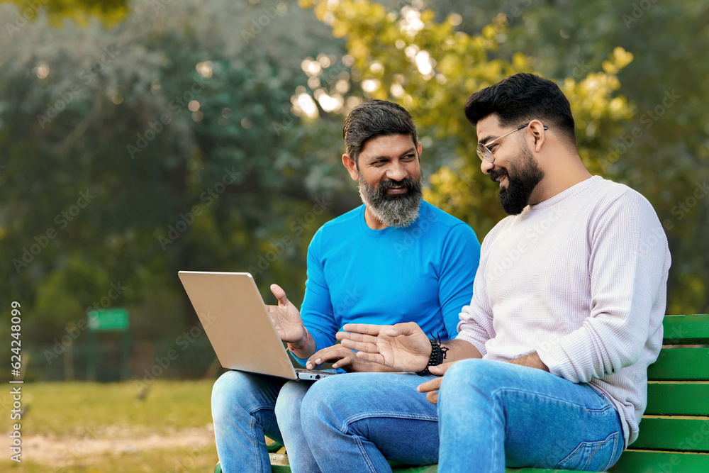 Two indian male discuss and using laptop at park Two indian male discuss and using laptop at park