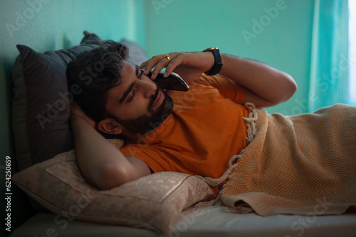 Young man talking on mobile phone while lying on bed