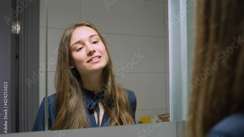 Happy brunette adjust hair against mirror in early morning, close up photo