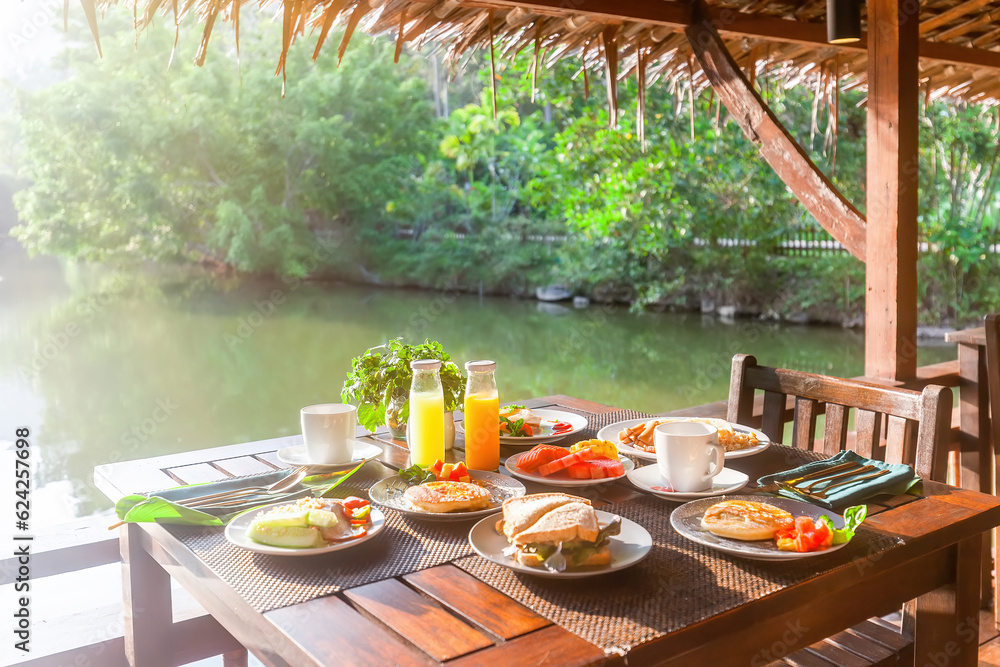 Enjoy a tropical breakfast near the lake in an Asian resort. Indulge in pancakes, sandwiches, coffee, juices, salad, fresh fruits. Healthy and tasty dishes for a Thailand vacation.