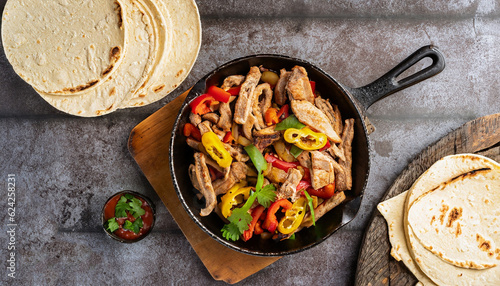 top down photo of mexican steak and chicken fajitas in iron skillet with corn tortillas