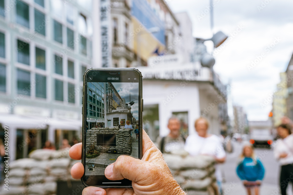 Naklejka premium Person taking a photo with an iphone at Check Point Charlie in Berlin, Germany