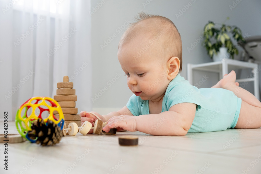 Cute little baby six months old in blue color bodysuit crawling on floor at home with light background and play wooden toys. Infant leisure at home. Cute little baby six months old in blue color bodysuit crawling on floor at home with light background and play wooden toys. Infant leisure at home.