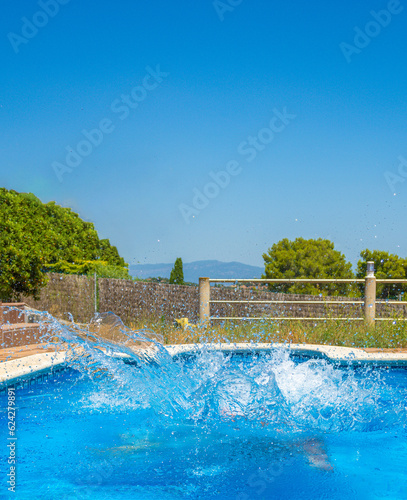 Waves and moving water inside a swimming pool after someone has jumped in causing splashing and splashing in a swimming pool of a luxury hotel resort on a sunny day with clear light blue sky © sirbouman