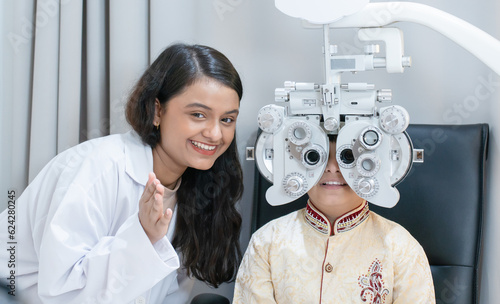 Ophthalmologist or optometrist or doctor doing eyes vision exam test for Indian child boy with diagnostic ophthalmology equipment, phoropter at hospital or optometry clinic. Eyes care in children