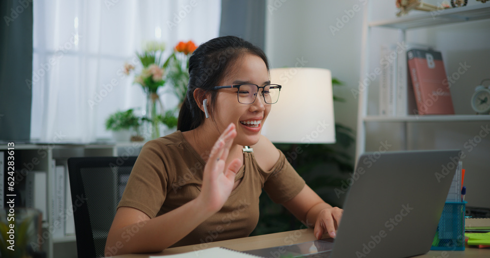 Happy young Asian woman wearing earphone doing video conference on a laptop Happy young Asian woman wearing earphone doing video conference on a laptop