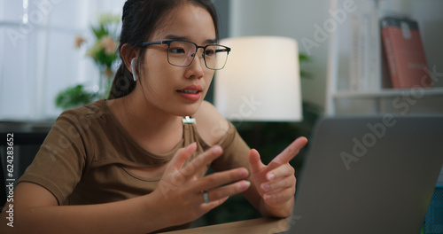 Happy young Asian woman wearing earphone doing video conference on a laptop