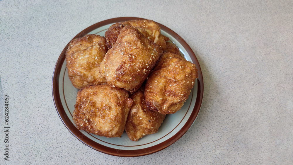 Roti goreng or Sweet fried bread sprinkled with sesame seeds on a plate on a ceramic surface, a simple Indonesian snack Roti goreng or Sweet fried bread sprinkled with sesame seeds on a plate on a ceramic surface, a simple Indonesian snack