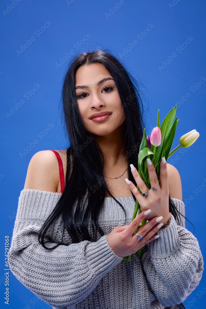 A beautiful young woman with tulips in her hand posing in the studio on a blue background A beautiful young woman with tulips in her hand posing in the studio on a blue background