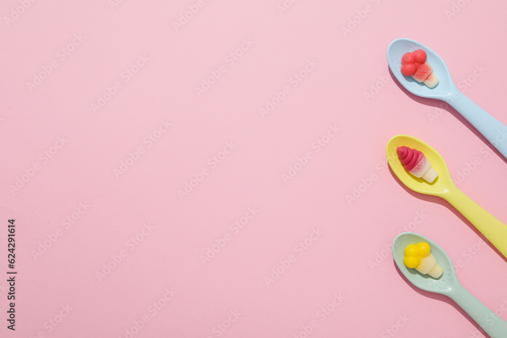 Jelly candies in spoons on pink background, space for text