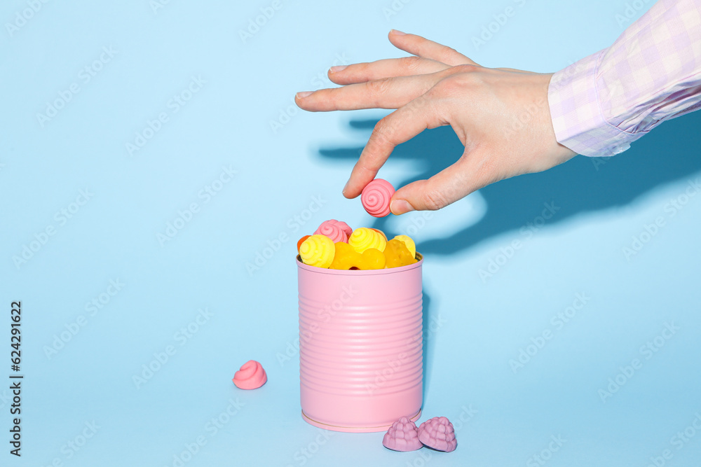 Jelly candies in purple tin and female hand on blue background Jelly candies in purple tin and female hand on blue background