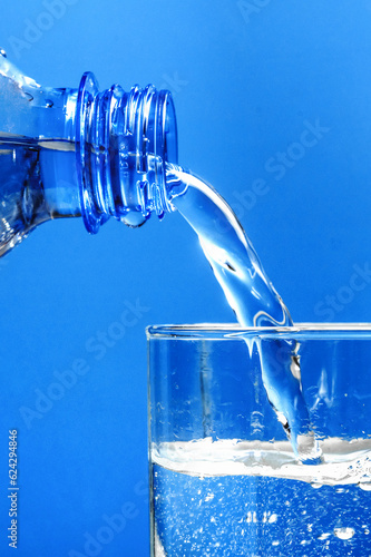 Pouring water from plastic bottle into glass on blue background. Stream of clean water flowing in a glass.