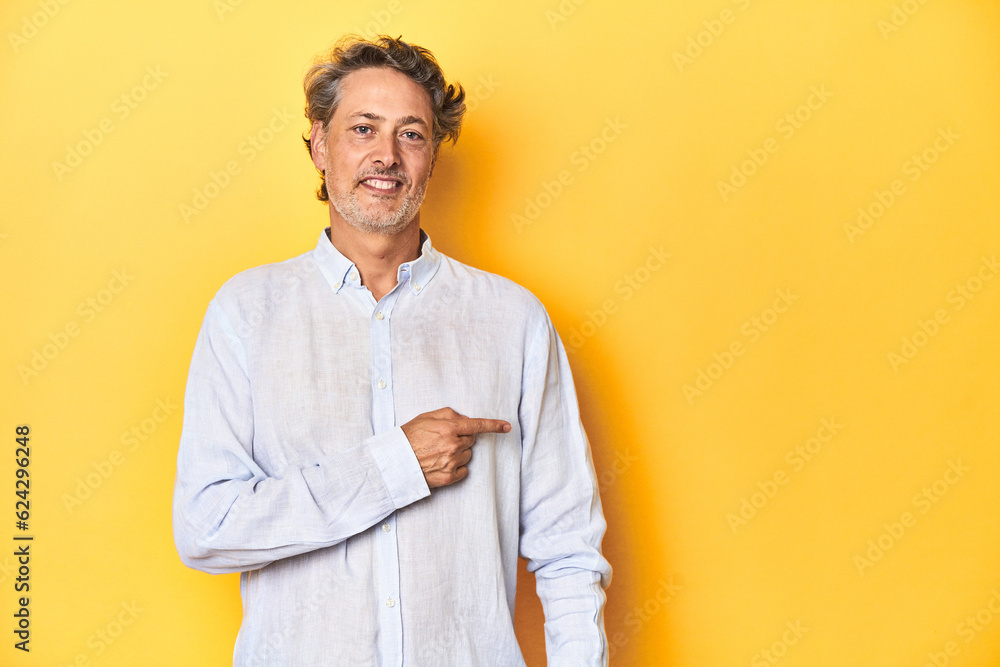 Middle-aged man posing on a yellow backdrop smiling and pointing aside, showing something at blank space. Middle-aged man posing on a yellow backdrop smiling and pointing aside, showing something at blank space.