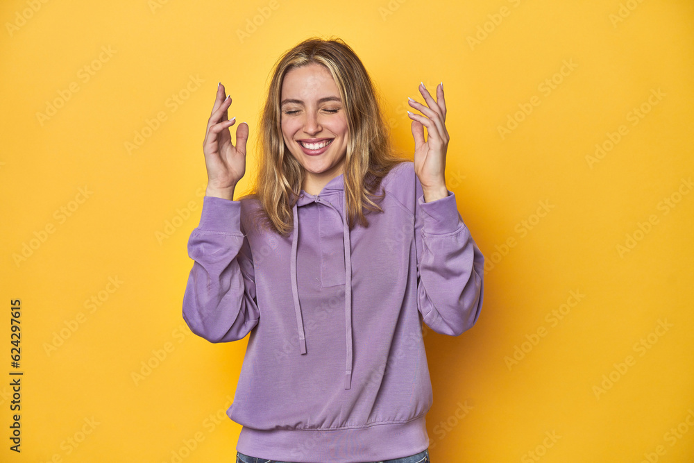 Young blonde Caucasian woman in a violet sweatshirt on a yellow background, joyful laughing a lot. Happiness concept. Young blonde Caucasian woman in a violet sweatshirt on a yellow background, joyful laughing a lot. Happiness concept.