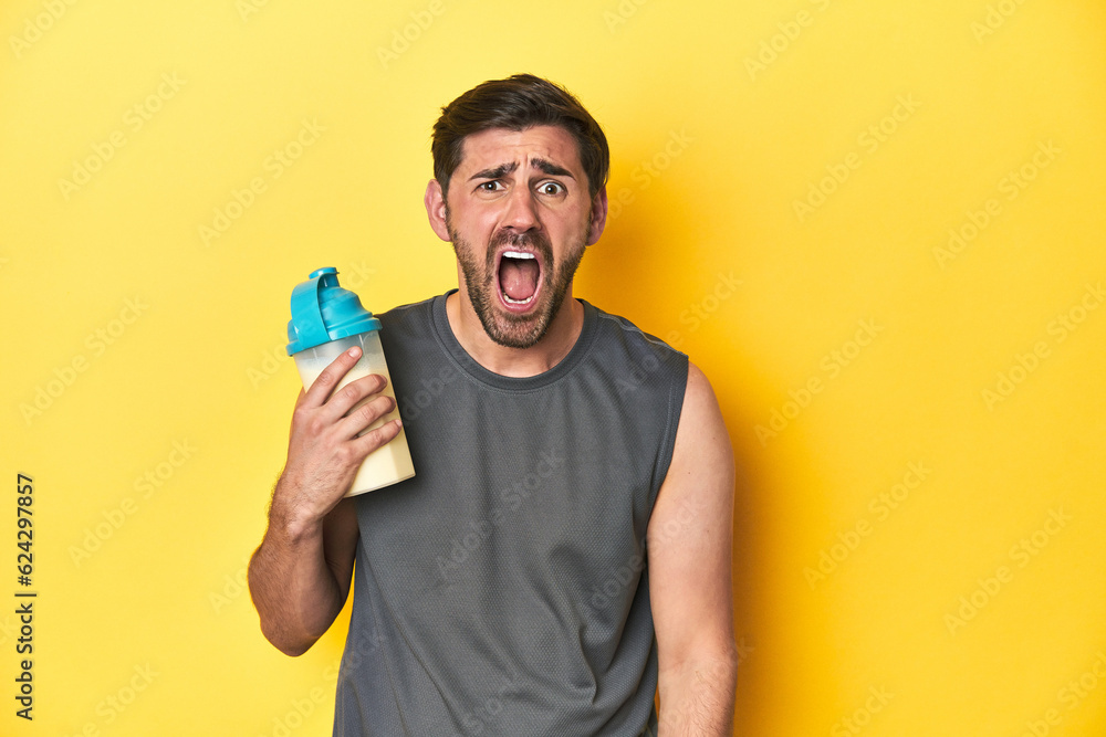 Fit man with protein shake, yellow studio background screaming very angry and aggressive. Fit man with protein shake, yellow studio background screaming very angry and aggressive.