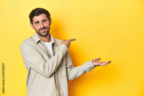 Caucasian man in grey shirt, studio shot on yellow excited holding a copy space on palm.