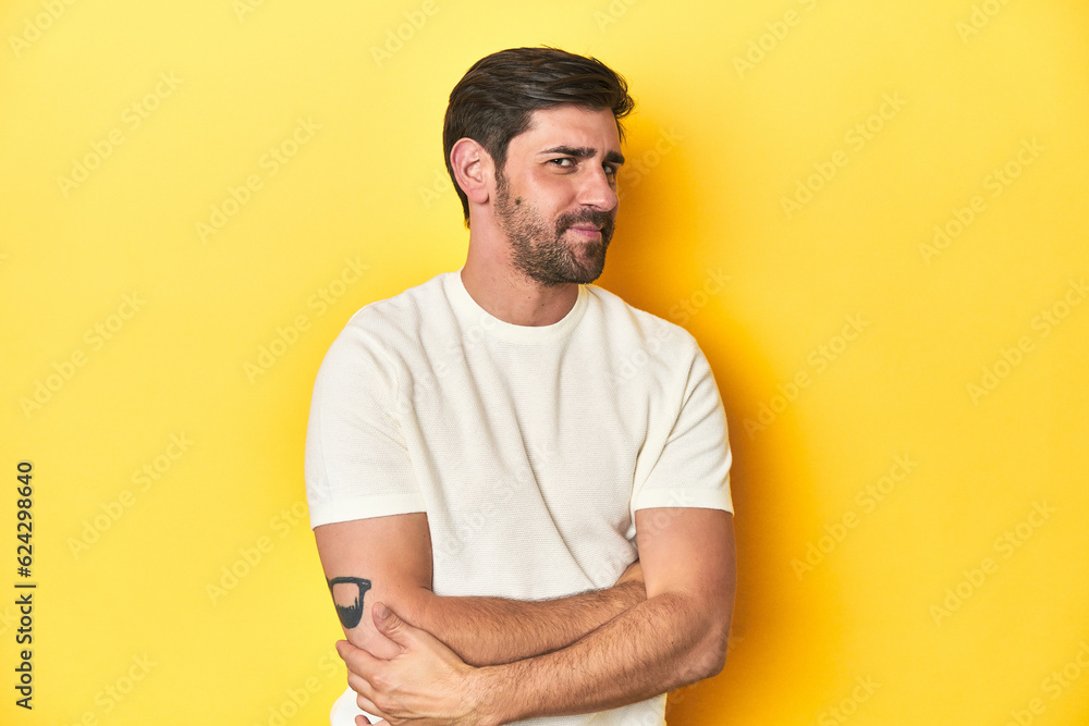 Caucasian man in white t-shirt on yellow studio background suspicious, uncertain, examining you. Caucasian man in white t-shirt on yellow studio background suspicious, uncertain, examining you.