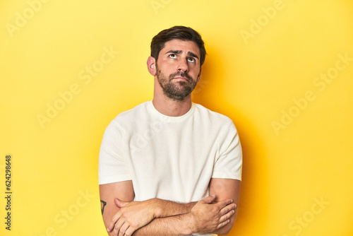Caucasian man in white t-shirt on yellow studio background tired of a repetitive task.