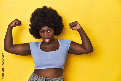 African-American woman with afro, studio yellow background raising fist after a victory, winner concept.