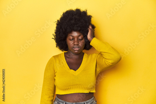 African-American woman with afro, studio yellow background tired and very sleepy keeping hand on head. © Asier