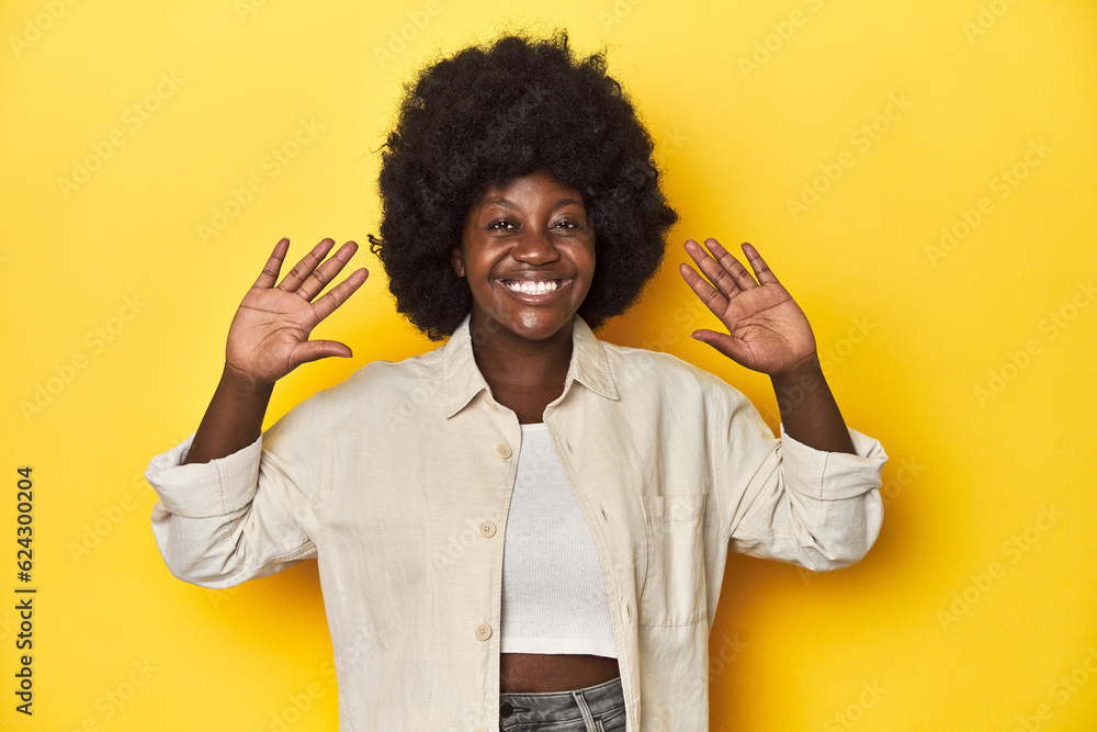 African-American woman with afro, studio yellow background showing number ten with hands. African-American woman with afro, studio yellow background showing number ten with hands.