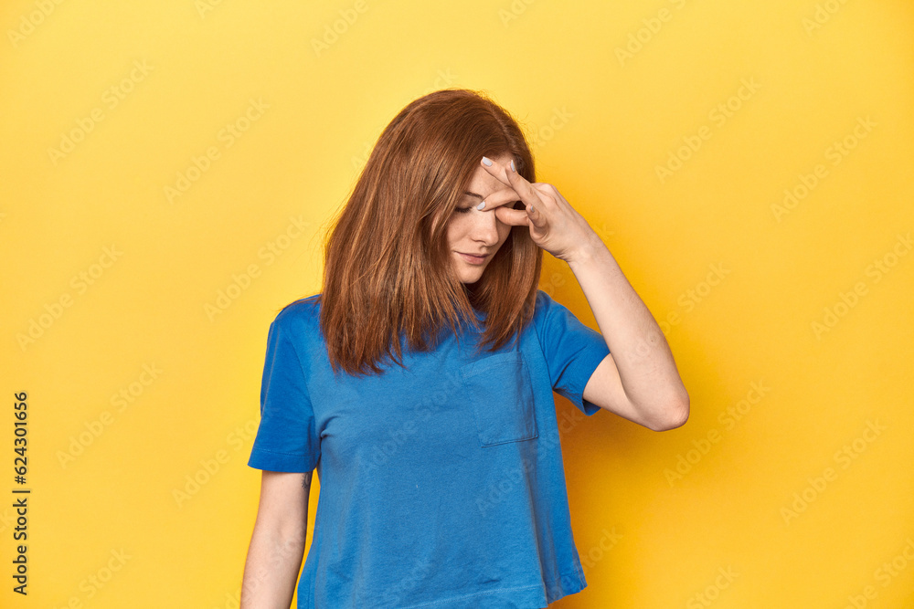 Redhead in blue t-shirt on yellow backdrop having a head ache, touching front of the face. Redhead in blue t-shirt on yellow backdrop having a head ache, touching front of the face.