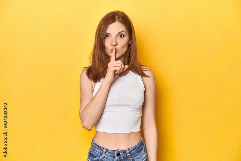 Redhead in white tank top, relaxed studio pose keeping a secret or asking for silence. Redhead in white tank top, relaxed studio pose keeping a secret or asking for silence.