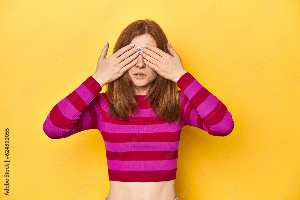 Redhead in pink-red striped shirt, casual look afraid covering eyes with hands. Redhead in pink-red striped shirt, casual look afraid covering eyes with hands.