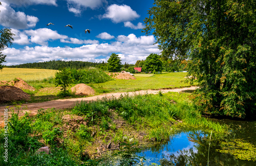 Countryside summer rural landscape with gravel road, river, green meadow  and...