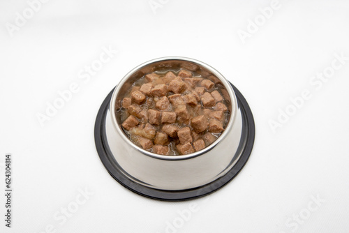 Wet cubical pieces pile isolated on white background. Bowl of meat dog food. Round metal bowl for pets with food.